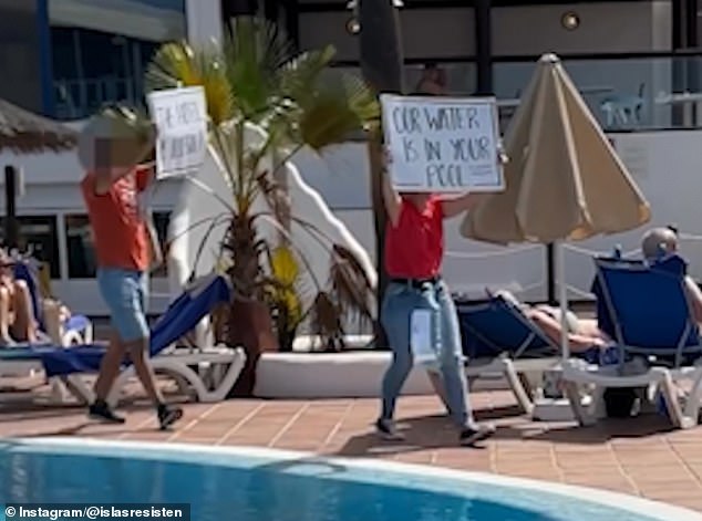 Protesters walk by the pool holding signs.