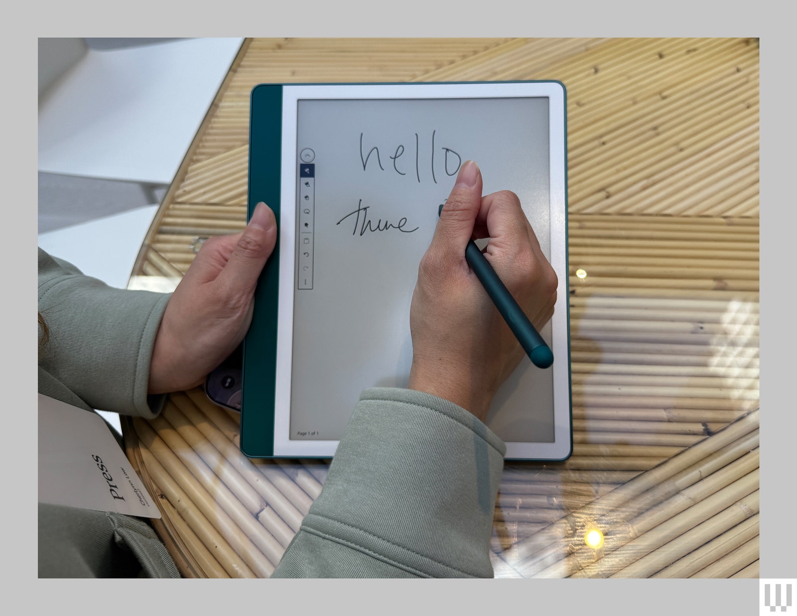 A person using a stylus to scribble on the screen of a Kindle Scribe, a teal e-reader with an interactive screen