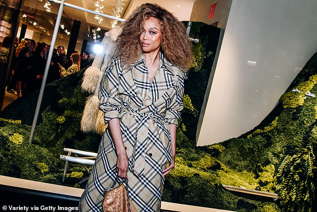 Tyra's long plaid trench coat was a departure from Burberry's shorter coats of recent years. She wore it with long white mule heels and carried a gold sequin bag.