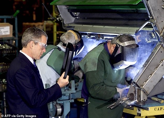 Former U.S. President George W. Bush (L) watches welders work on a John Deere combine during a factory tour on January 14, 2002 in Moline, Illinois.