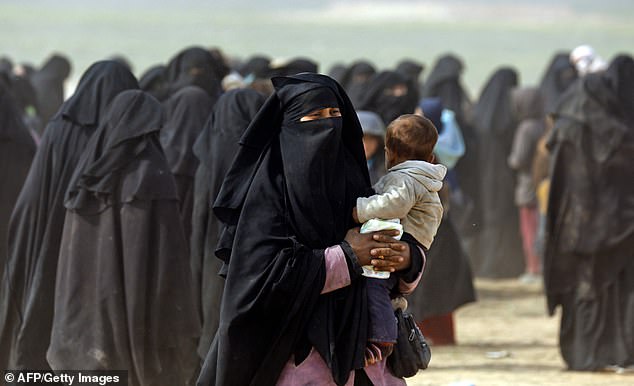 A fully veiled woman holds her baby as civilians fleeing the Islamic State group in Baghouz walk through a field on February 13, 2019.