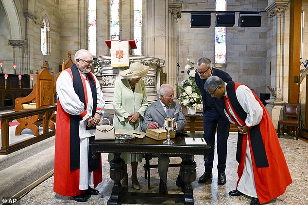 King Charles signs a copy of the Bible as Queen Camilla looks on during a visit to St Thomas' Anglican Church.