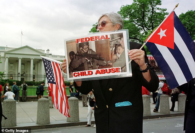 A member of Mothers Against Repression holds a photograph showing a federal agent with an automatic rifle confronting fisherman Donato Dalrymple holding Elián González in a closet during a demonstration in front of the White House on April 26, 2000 Washington, DC