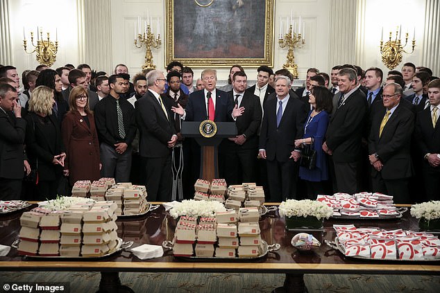 Then-President Donald Trump speaks behind a table filled with McDonald's burgers, Chick fil-a sandwiches and other fast foods as he welcomes the 2018 Division I Football FCS champions, the North Dakota State Bison, in the Diplomatic Room of the White House on March 4, 2019. In Washington, DC, COVID protocols affected kitchens at the time.