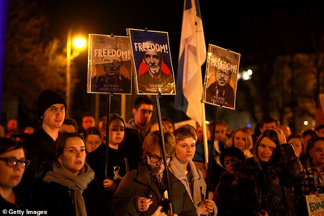 People hold banners during a vigil in memory of Alexiei Navalny in front of the Russian Consulate General on February 16, 2024 in Munich, Germany.