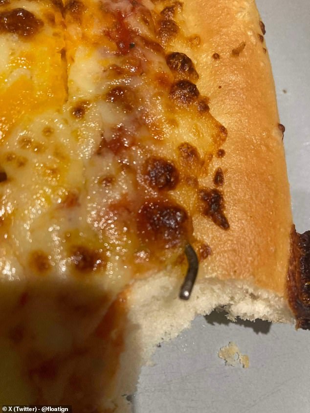 A close-up photo of the food shows the metal hook cooked into the pizza, beneath a layer of cheese.