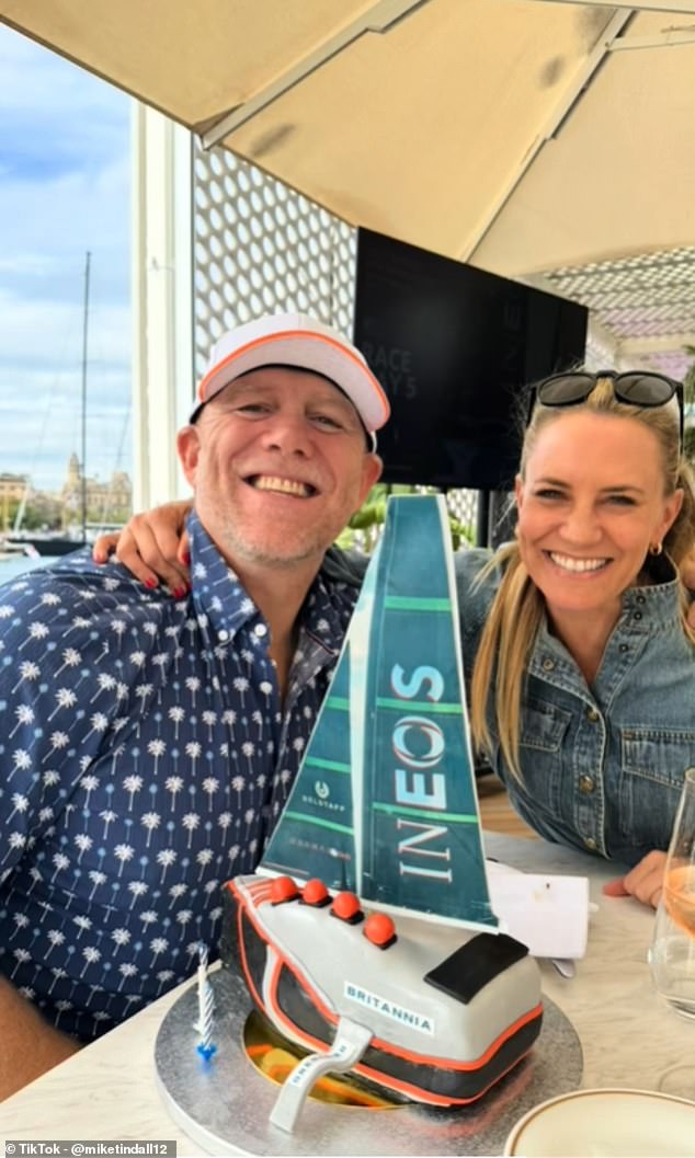 A candid snap shows Mike flashing a smile as he poses next to an Ineos Britannia-themed birthday cake in the shape of a yacht, complete with candles and orange buoys made of icing.