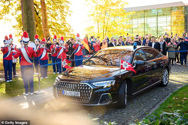 The Danish royal couple arrives in a blacked-out Audi adorned with Danish flags as a brass band dressed in red, white and blue plays to welcome them.