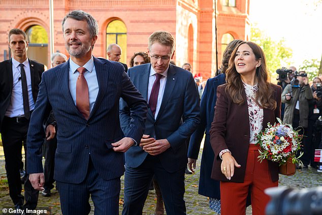 Her husband, King Frederik (left), looks dapper in a navy striped suit, complete with a crisp light blue shirt, polished black shoes and an amber patterned tie.