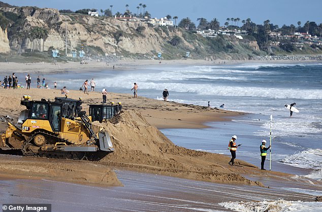 Workers measure sand elevation along fresh sand during a sand replenishment project