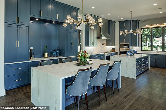 The kitchen area contains two islands, as well as blue cabinets and two modern light fixtures hanging from the ceiling.