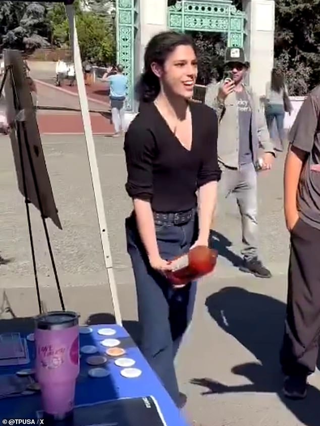 The person can be seen pouring the juice on his signage and his table, which is covered in badges and posters.