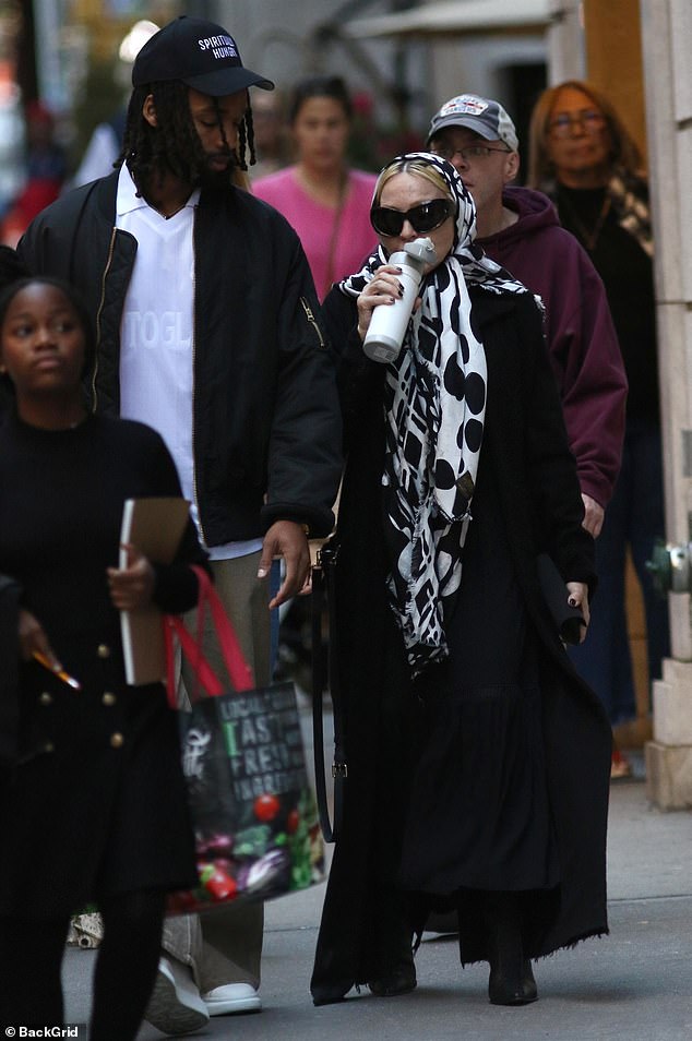 She wore a long black trench coat and dress and hid her bleached locks with a printed scarf. The brand paired its cozy look with oversized designer sunglasses.