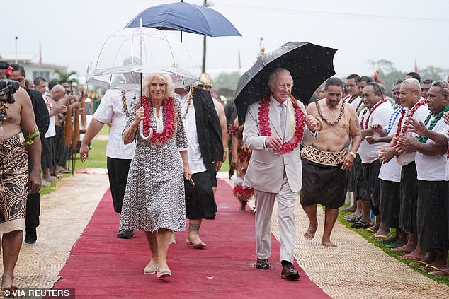 The couple, umbrellas in hand, walked down a soggy red carpet to a stage that had been covered with woven mats and adorned with flowers.