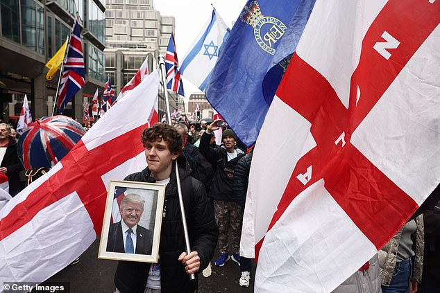 A young man holds a photo of Donald Trump as he marches through London as part of the crowd.