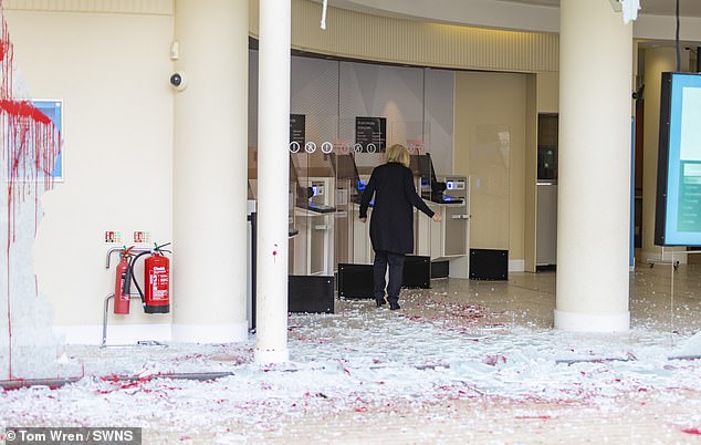 A woman in Bristol carefully picks her way over the broken and stained glass of a Barclays branch.