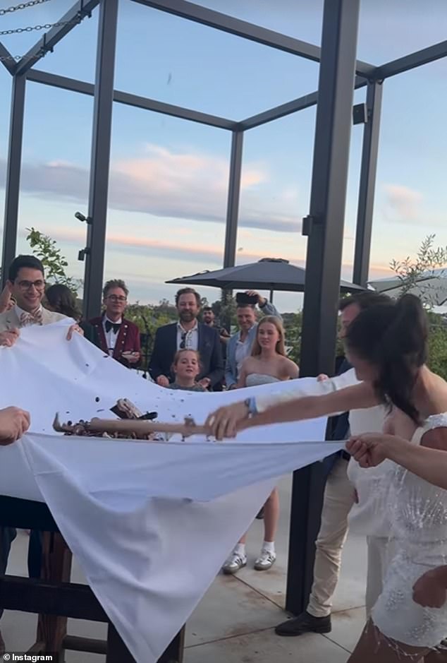 The newlyweds were definitely in good spirits, happily attacking a two-tier chocolate cake which they smashed with a cane while an entourage of guests looked on.