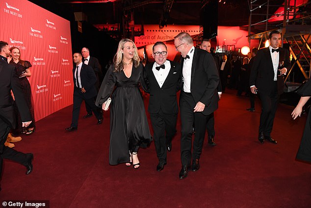 Former Qantas CEO Alan Joyce walks proudly down the red carpet with one arm around the Prime Minister and the other around his partner Jodie Haydon.