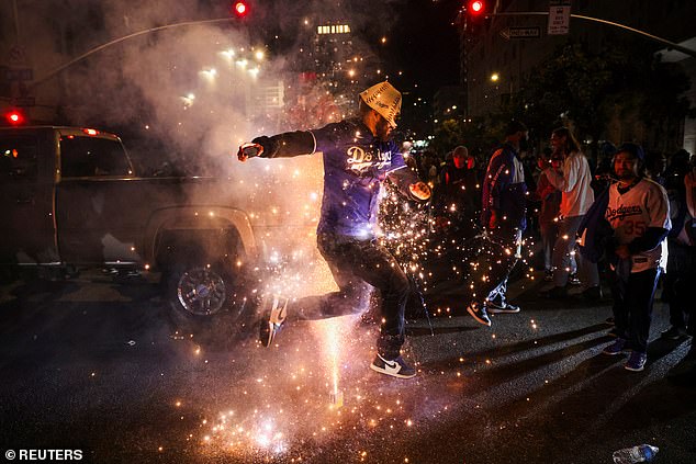 A fan in a Dodgers jersey jumps over a firework at wild celebrations in Los Angeles.