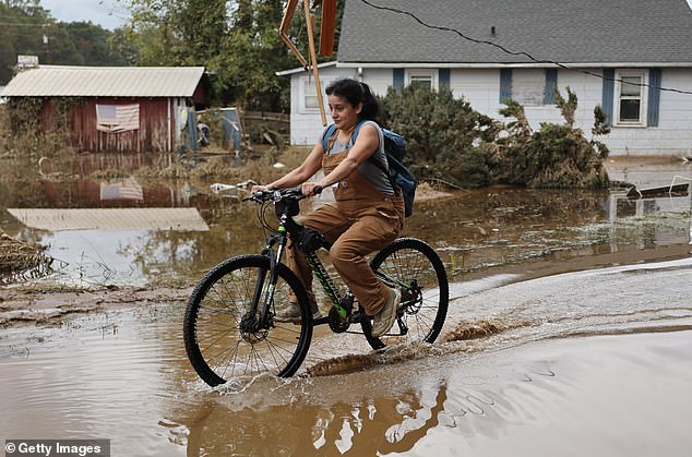 A person rides a bicycle through floodwater left over from Hurricane Helene on October 4, 2024 in Swannanoa, North Carolina.