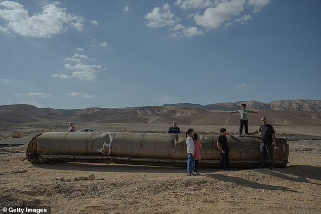 People take photos and stand on the remains of a missile in Israel