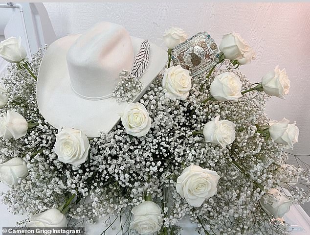 The coffin was covered with a white cloth beneath a bouquet of white roses and baby's breath. The arrangement was accessorized with a silver belt buckle and a white western hat.