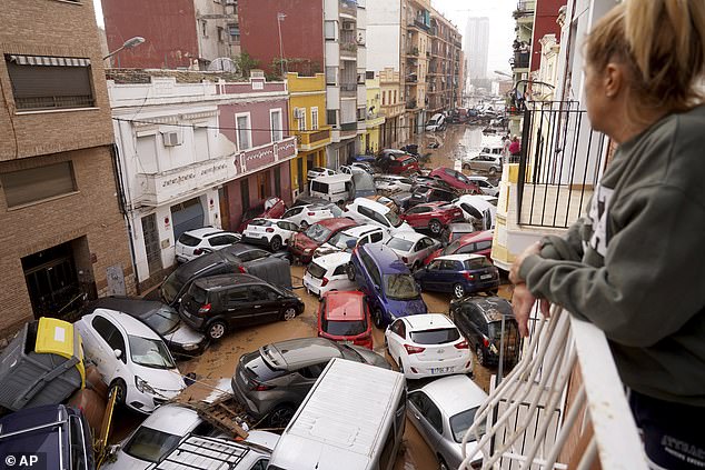 A woman watches from her balcony as vehicles are trapped in the street during floods in Valencia