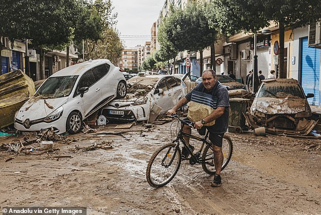 A man cycles past broken down cars in the Sedavi district of Valencia, it is estimated that more than 100,000 homes are currently without electricity in the region