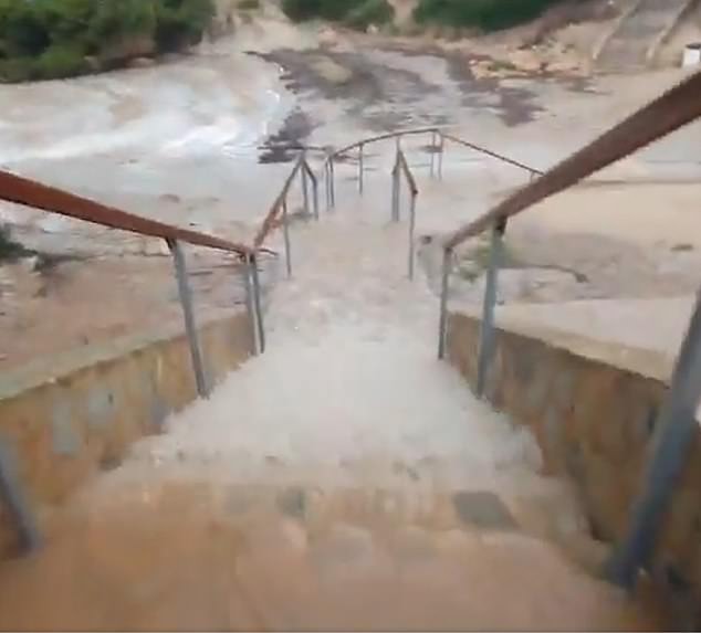 Water runs down stairs in a town in Mallorca while roads are submerged by heavy flooding.