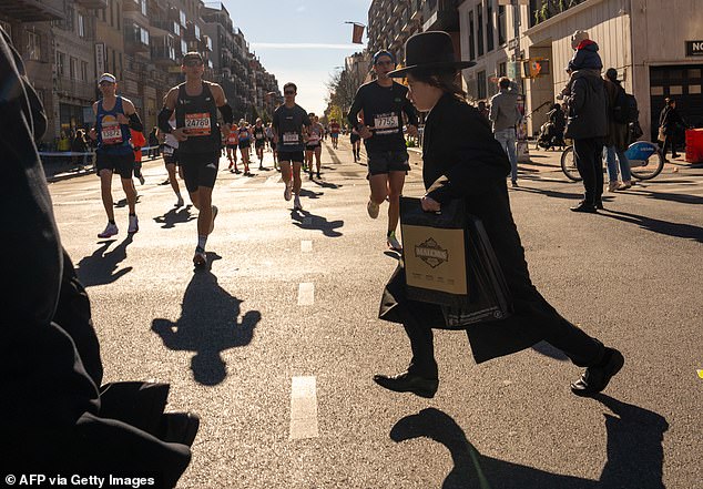 A boy runs across the street as New York City marathon runners make their way down the course.