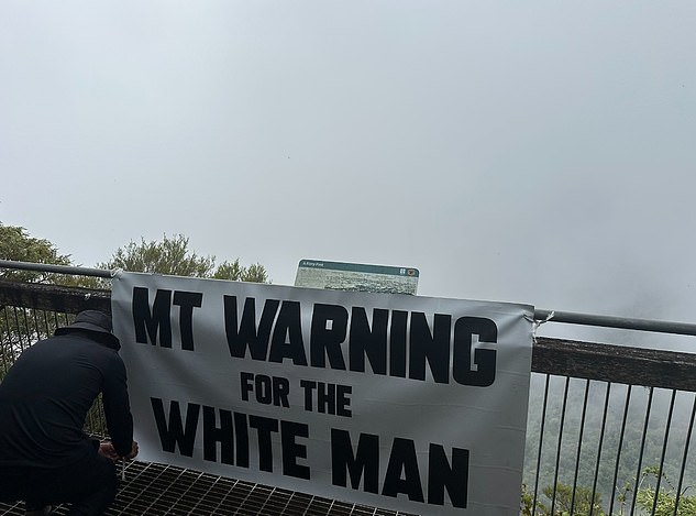 A black-clad and masked member of the group was seen tying the sign to the overlook fence.