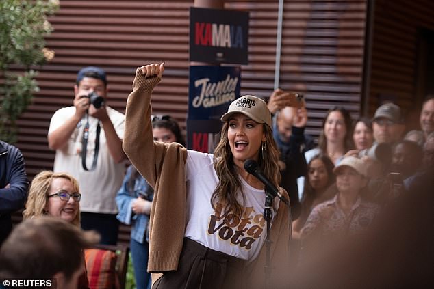 Alba looked upbeat on the microphone at the event in a white 'Vote' t-shirt that she covered with a comfortable brown cardigan while wearing dark brown high-waisted pants and a Harris-Walz baseball cap.