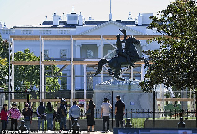 Passersby stand in front of a fence on the White House grounds.