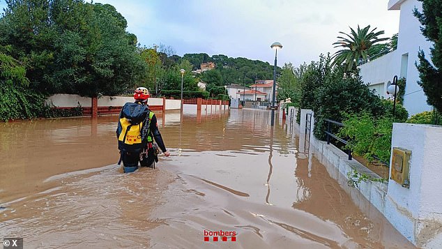 An emergency worker is seen walking through flooded waters in Catalonia this morning.