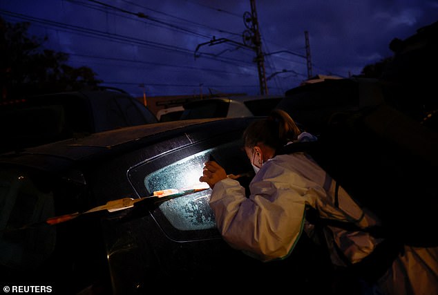 A police officer inspects the inside of piled-up vehicles for victims following Saturday's flooding.