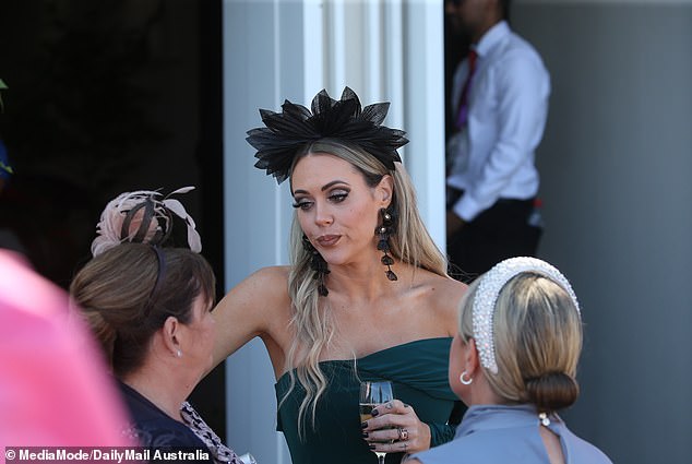 Her blonde hair was styled sleek and straight, with a bold, oversized black fascinator crowning her look—a classic touch of race day style.