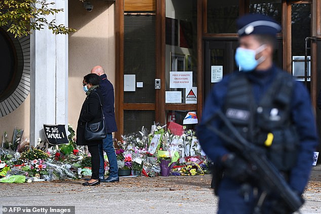 People look at flowers placed in front of Bois d'Aulne High School in honor of murdered history teacher Samuel Paty, who was beheaded by an attacker for showing students caricatures of the Prophet Muhammad in his civics class, on 19 October 2020, in Conflans. Sainte-Honorine, northwest of Paris. Eight people between 22 and 65 years old will appear before the special court in Paris starting November 4, 2024