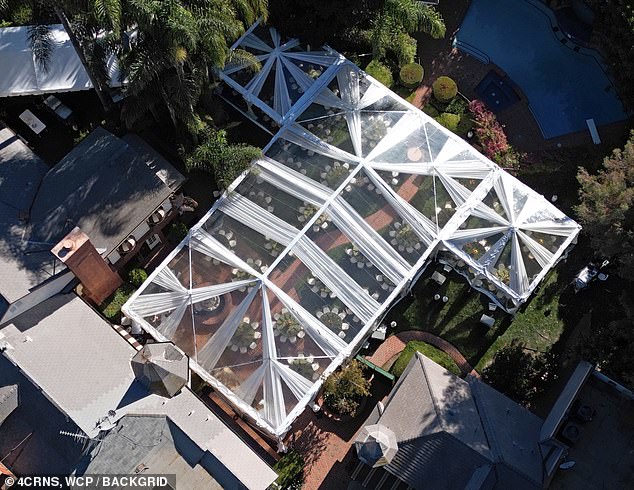 Behind the house a large tent with a transparent roof was set up and several circular tables and chairs were placed underneath for the guests.