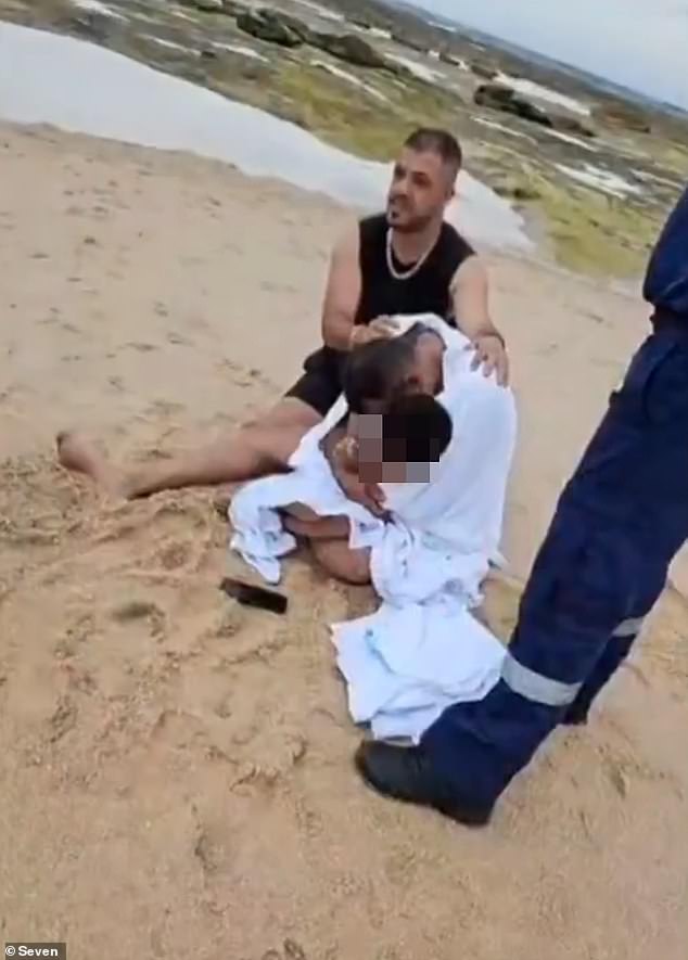 The distraught father was later photographed sitting on the sand hugging his youngest son tightly as he was comforted.