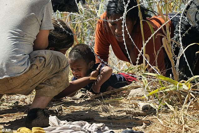 Migrants who crossed into the United States from Mexico pass under barbed wire along the Rio Grande River