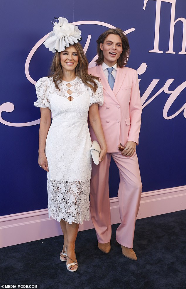 Liz looked glamorous in a white midi dress while Damian sported a pink suit and blue satin tie.