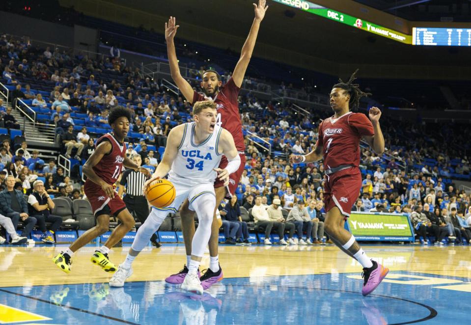 UCLA forward Tyler Bilodeau passes under the basket near two Rider players