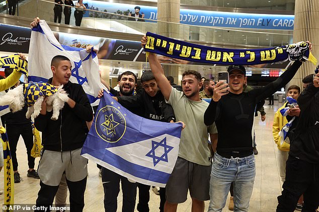 Maccabi Tel-Aviv fans carry flags as they wait for their friends and family to arrive from Amsterdam at Ben Gurion International Airport.