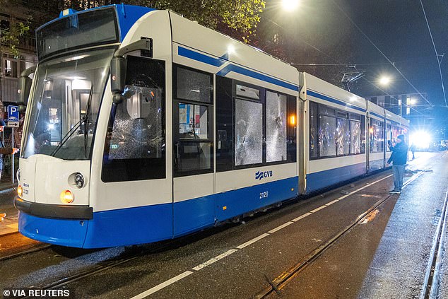 A man stands next to the tram, whose windows have been smashed during the riots.