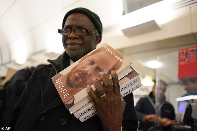 A customer holds up copies of 'Spare' in a London bookstore during a midnight opening in 2023.