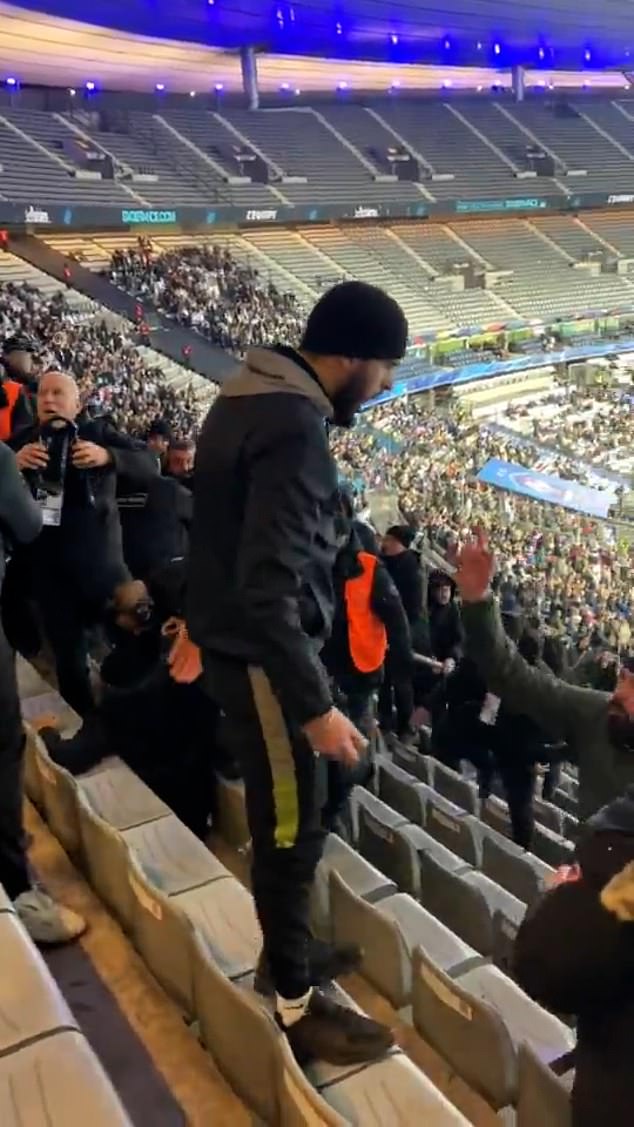 One man, wearing a hat, stands on one of the chairs and shouts aggressively at people nearby