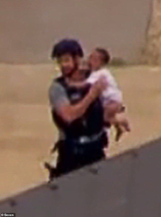 Television footage from a helicopter captured the dramatic moment the boy was rescued from the house and placed in the arms of an armed police officer (pictured).