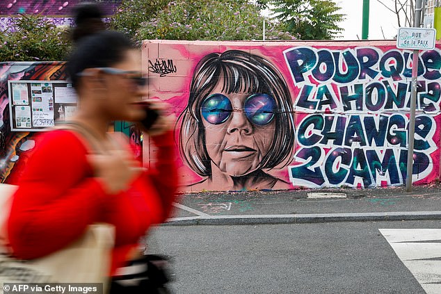 A woman walks past a mural created by Maca_dessine depicting Gisele Pelicot and a phrase reading 