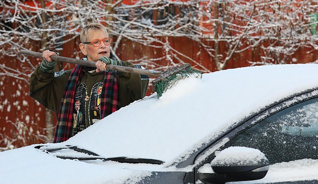 Shannon Finlayson uses a broom to remove snow from the windscreen of her car in Inchbae, Wester Ross Scotland