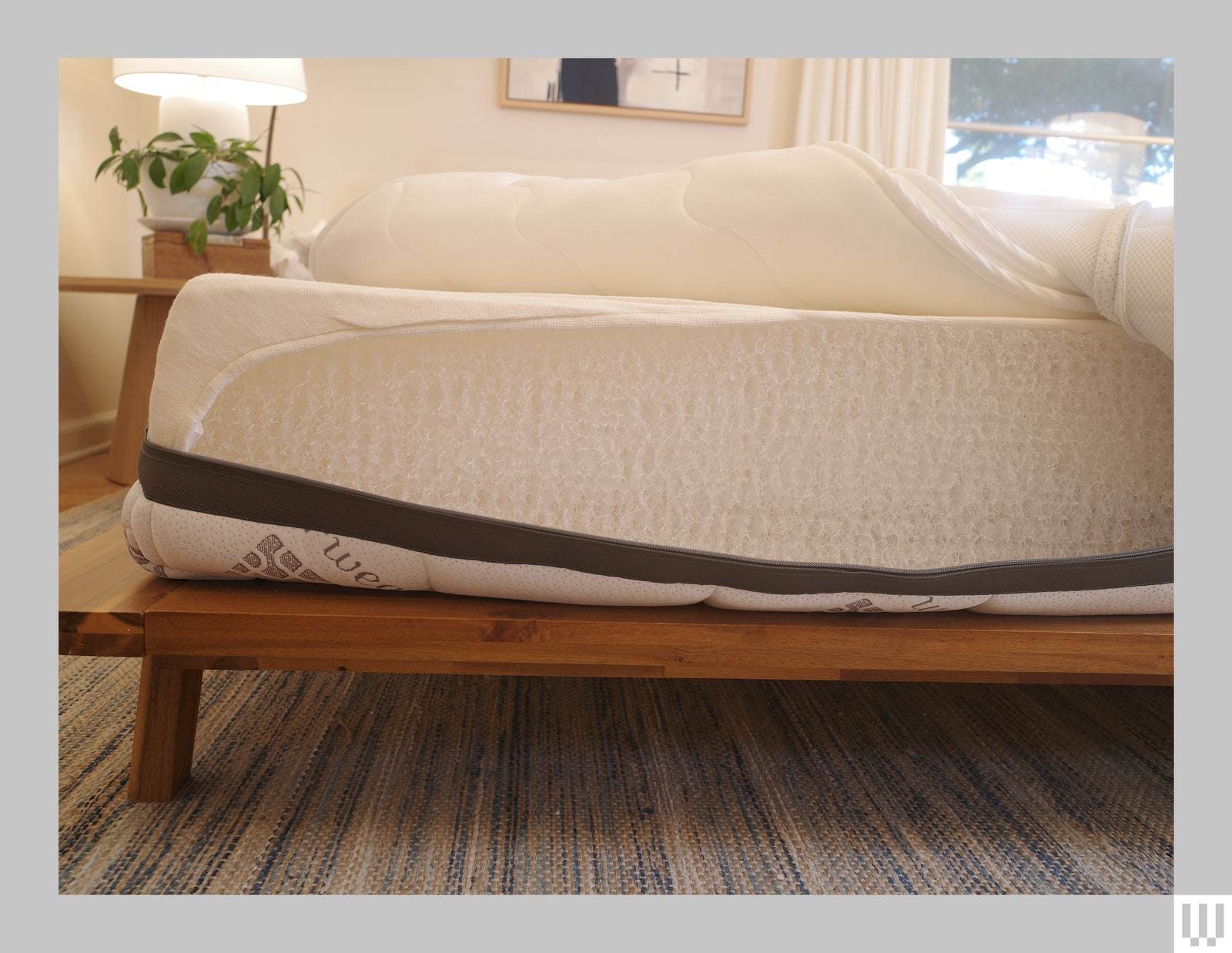 Corner view of Airweave bed on a minimalist wooden platform with the cover open to show the inner mesh layers